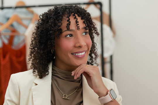 Woman standing in fashion boutique holding muted rust dresses on clothing rack, copy space