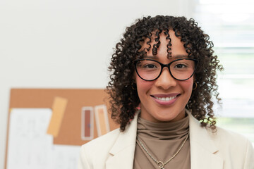 Mid adult African American woman wearing blazer smiling by corkboard in office reviewing sketches