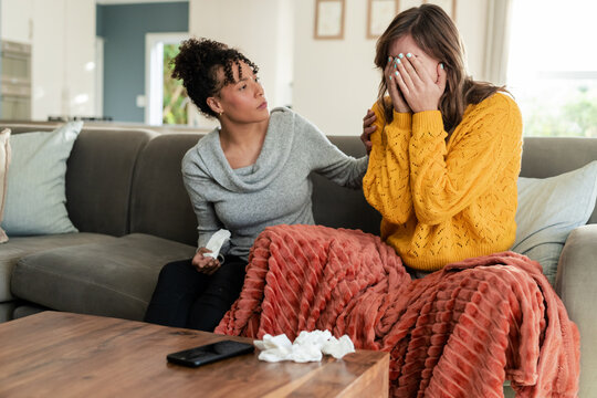 Diverse female friends comforting tearful companion on sofa with blanket and tissues, copy space