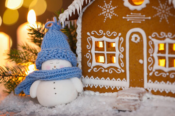 Beautiful gingerbread house and cute decorative snowman on table against blurred lights, closeup....