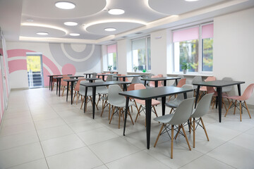 Tables with chairs in stylish room at school