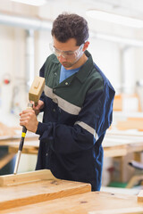 Carpenter is chiseling rectangular plank on workbench in workshop with mallet, chisel and sawdust