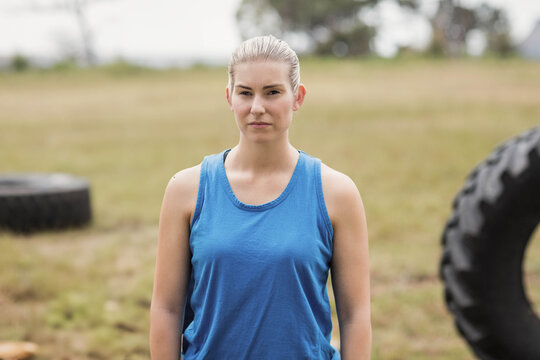 Woman standing facing camera in open grassy field wearing blue sleeveless tank top near tires