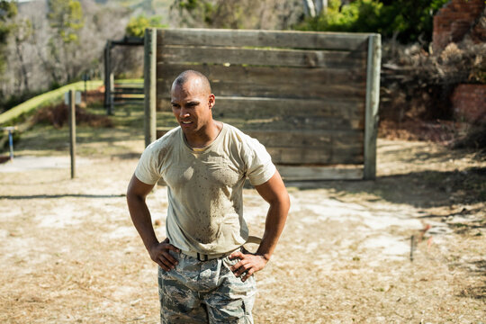 African American mid adult man standing hands on hips at wooden obstacle wall wearing camo trousers - Powered by Adobe
