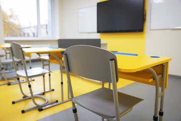 Stylish classroom with desks, chairs and tv at school, selective focus