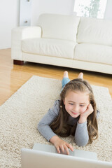 School-age girl lying on beige shag rug at home using silver laptop under window light