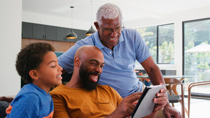 Multi-Generation Male African American Family Sitting On Sofa At Home Using Digital Tablet