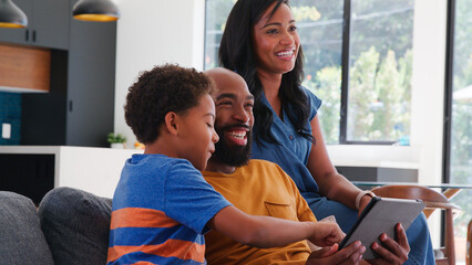 African American Father And Son Sitting On Sofa At Home Using Digital Tablet