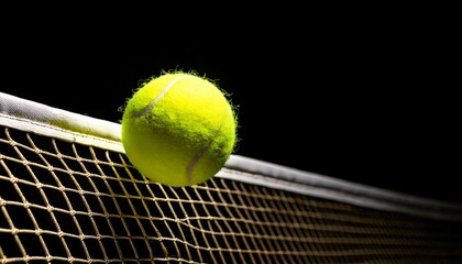 Yellow tennis ball hangs poised above a dark tennis net