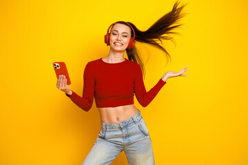Young woman wearing red crop top and headphones smiling and dancing against bright yellow background for lifestyle fashion stock photo