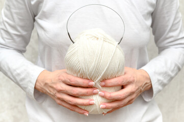 A woman in a white blouse holds white yarn with knitting needles in her hands.