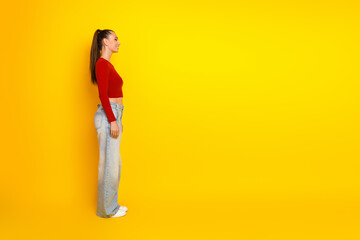 Young woman in red top and jeans stands in profile against a bright yellow background for fashion lifestyle and advertising