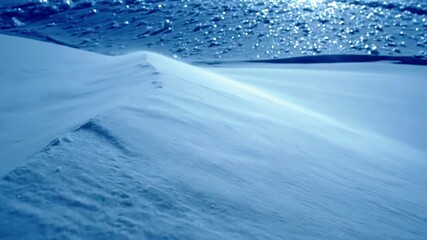 Windblown snow drifts across a sunlit slope, forming soft ridges and sparkling ice blue minimalist winter landscape with motion and texture. - Powered by Adobe