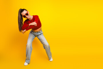 Young woman in red top and jeans dancing against a bright yellow background conveying fun and fashion style