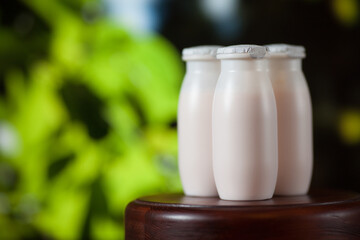 Natural liquid yogurt with probiotics in small plastic bottles on wooden table on background of green trees on a sunny day. Healthy, balanced diet food, healthy breakfast, dairy products.