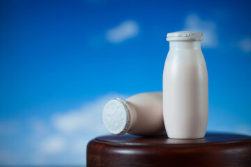 Natural liquid yogurt with probiotics in small plastic bottles on wooden table on background of blue sky with clouds. Healthy, balanced diet food, healthy breakfast, dairy products.