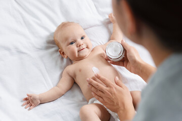 Mother applying cream onto baby's skin on bed at home, above view