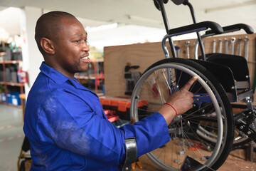 Mid adult African American tech in blue coverall inspecting wheelchair on workbench, copy space