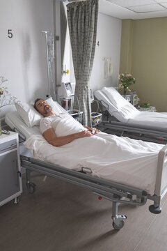 Male patient reclining in hospital bed wearing white T-shirt and receiving IV via pole and pump