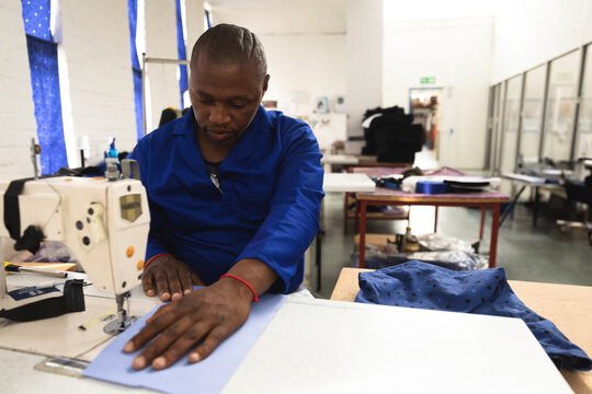Mid-adult African American man in blue jacket sewing blue fabric on industrial machine in workshop