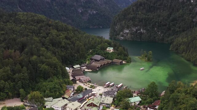 Aerial view of KOnigssee lake surrounded by green trees and boathouses, creating a vibrant contrast with the water's dark depths, Schoenau am Koenigssee, Bavaria, Germany.
