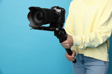 Videographer using gimbal stabilizer with camera on light blue background, closeup