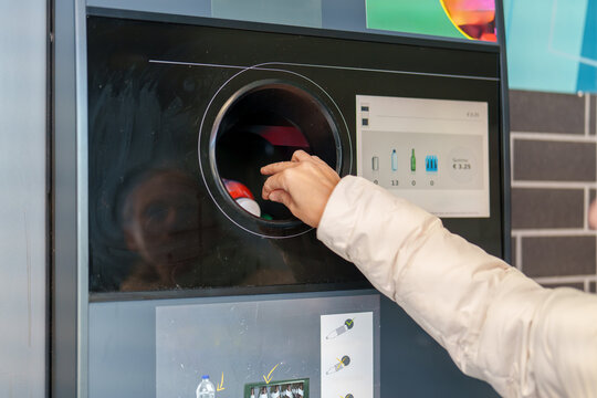 Person returns bottles at a bottle recycling machine in a public space during daylight hours