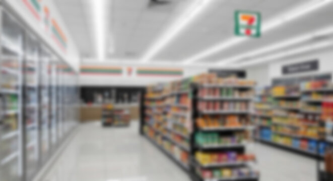 Blurred interior of a modern supermarket or convenience store aisle, with shelves full of products. Suitable for retail, shopping, or promotional background designs.