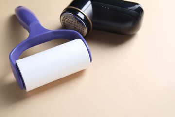 Lint roller and fabric shaver on beige background, closeup. Space for text