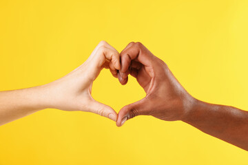 African American man making heart gesture with his partner on yellow background, closeup