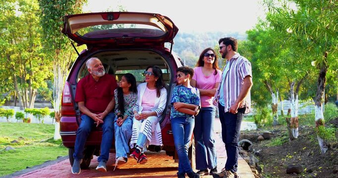 Indian family sitting in car dicky outdoors ready to go for picnic enjoying fun moments, grandparents, parents, and kids relaxing together, sharing laughter and bonding during a joyful outdoor break
