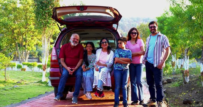Indian family sitting in car dicky outdoors ready to go for picnic enjoying fun moments, grandparents, parents, and kids relaxing together, sharing laughter and bonding during a joyful outdoor break