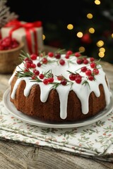 Delicious Christmas cake with icing, cranberries and rosemary on wooden table against black background with blurred lights. Bokeh effect