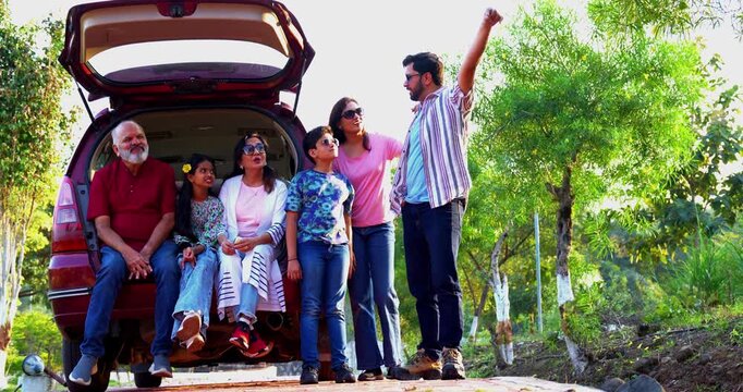 Indian family sitting in car dicky outdoors ready to go for picnic enjoying fun moments, grandparents, parents, and kids relaxing together, sharing laughter and bonding during a joyful outdoor break