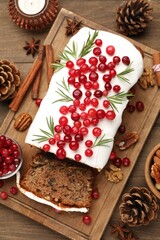 Tasty Christmas cake with icing, cranberries and rosemary on wooden table, flat lay