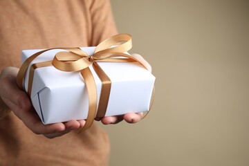 Woman with gift box on beige background, closeup. Space for text