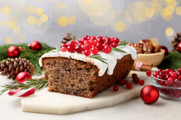 Tasty Christmas cake with icing, cranberries, nuts and festive decor on light grey table against blurred lights, closeup. Bokeh effect