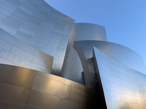 LOS ANGELES, CA, OCT 1, 2025: Dramatic metallic surface of Walt Disney Concert Hall with sweeping curves and sharp angles, golden light warming lower sections against cool silver tones above