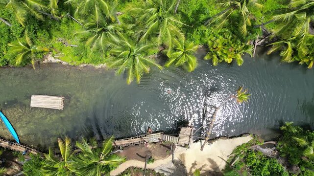 Aerial view of the river flanked by lush greenery, with a small dock and raft, the water reflecting the sunlight, Dapa, Caraga, Philippines.