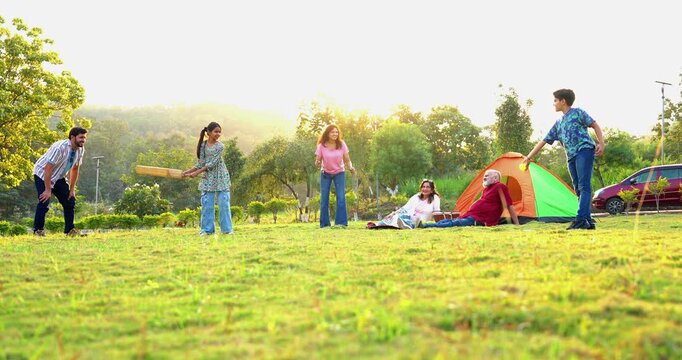 Indian family playing cricket while camping outdoors, enjoying fun bonding moments, laughter, teamwork, and relaxed weekend togetherness
