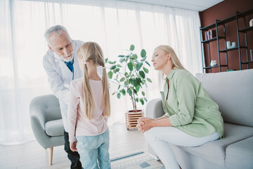 Obraz premium A friendly doctor talks with a mother and her young daughter in a bright living room during a home health visit showing care trust and family support in a calm modern setting