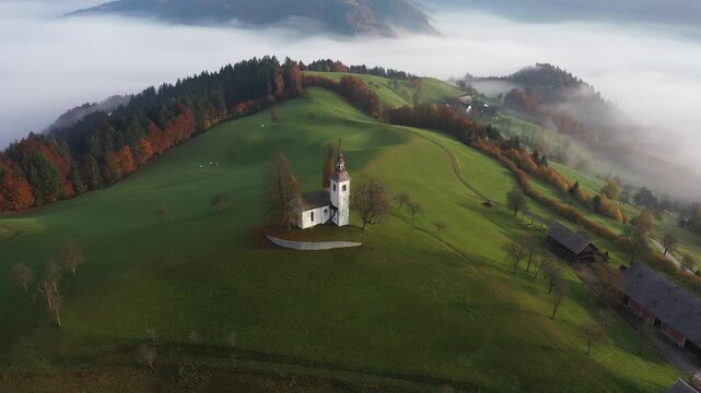 Aerial view of a white church nestled in the vibrant green field, juxtaposed against the colorful autumn foliage, Sv.Tomaz, Ormoz, Slovenia.