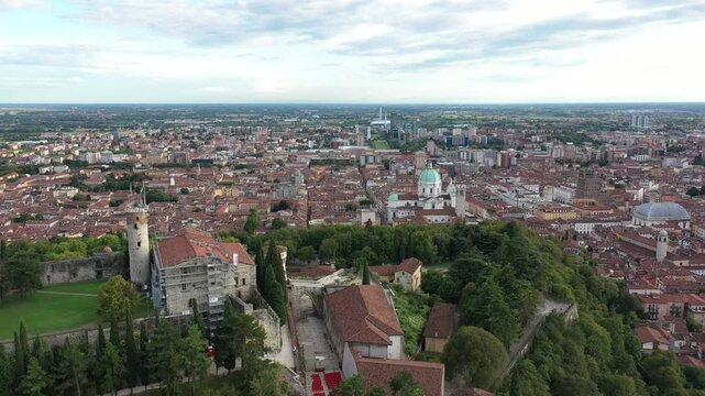 Aerial view of Brescia Castle on a lush green hill with the cityscape sprawling in the background, Brescia, Lombardy, Italy.