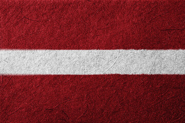 A textured, close-up shot presents the flag of Latvia, featuring two dark carmine stripes separated by a central white band, evoking a sense of national pride and cultural identity