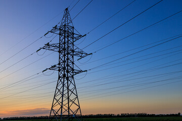 A tall power tower with many wires is silhouetted against a blue sky