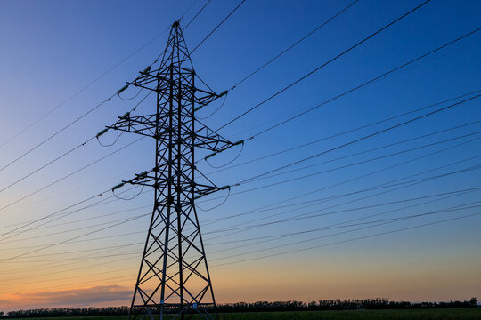 A tall power tower with many wires is silhouetted against a blue sky