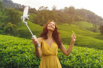 Woman Taking Selfie Holding Tea Leaf in Scenic Plantation at Sunset