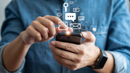 Hands holding smartphone with floating icons messages, email, social media, keys; blue denim shirt background, modern mobile technology, digital connection, soft blurred lighting.