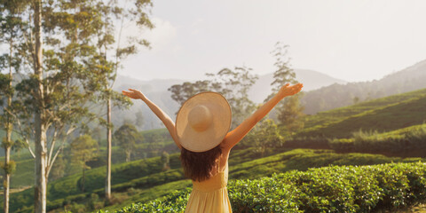 Woman in Straw Hat Enjoying Sunrise Over Tea Plantation with Open Arms