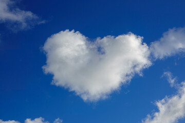 fluffy white cloud shaped like a heart floats against a bright blue sky